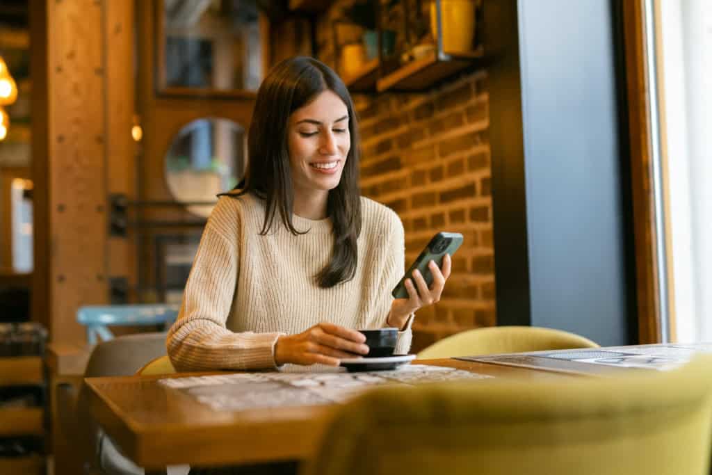 Woman enjoying a coffee while smiling at her phone in a café.