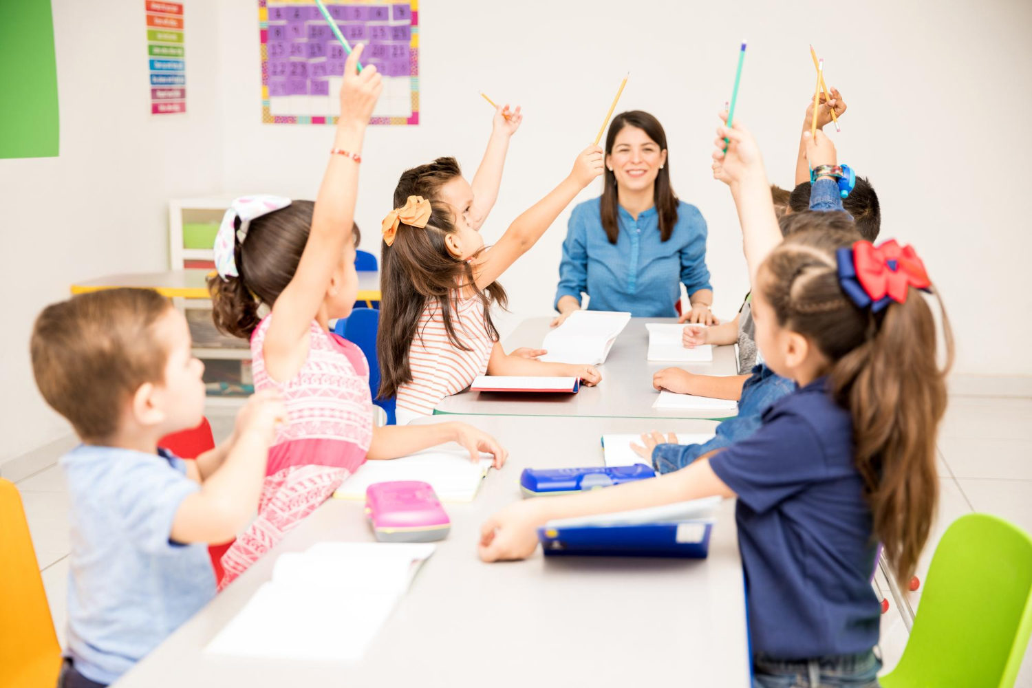 Un miembro del personal de la guardería observa a los niños levantar la mano en un aula.