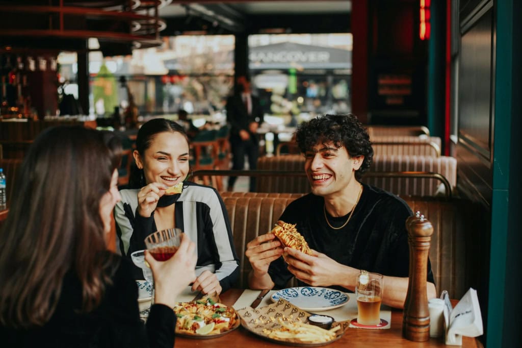 Three people enjoying food and laughing together at a restaurant.