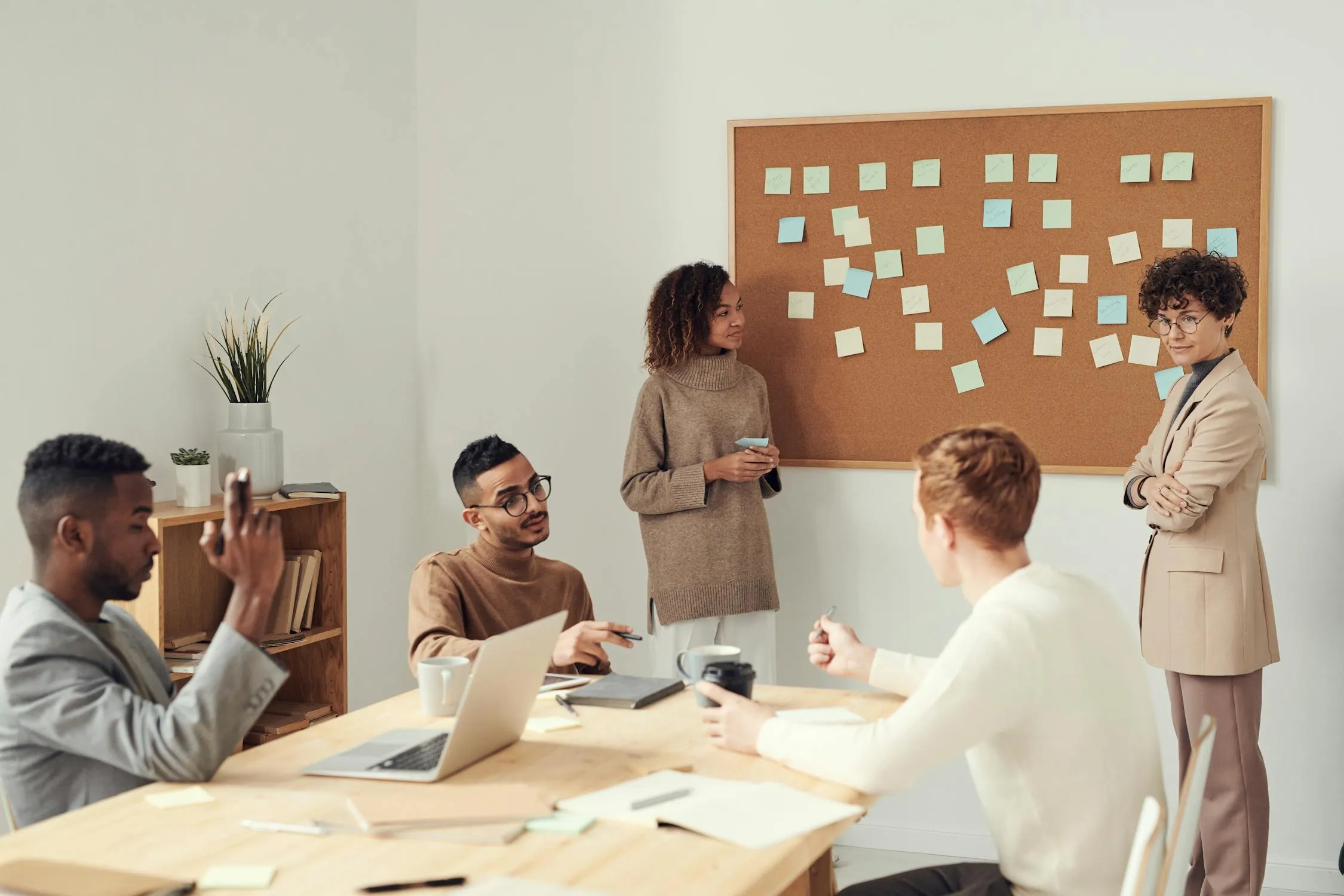 Team planning a presentation structure with sticky notes on a corkboard during a meeting