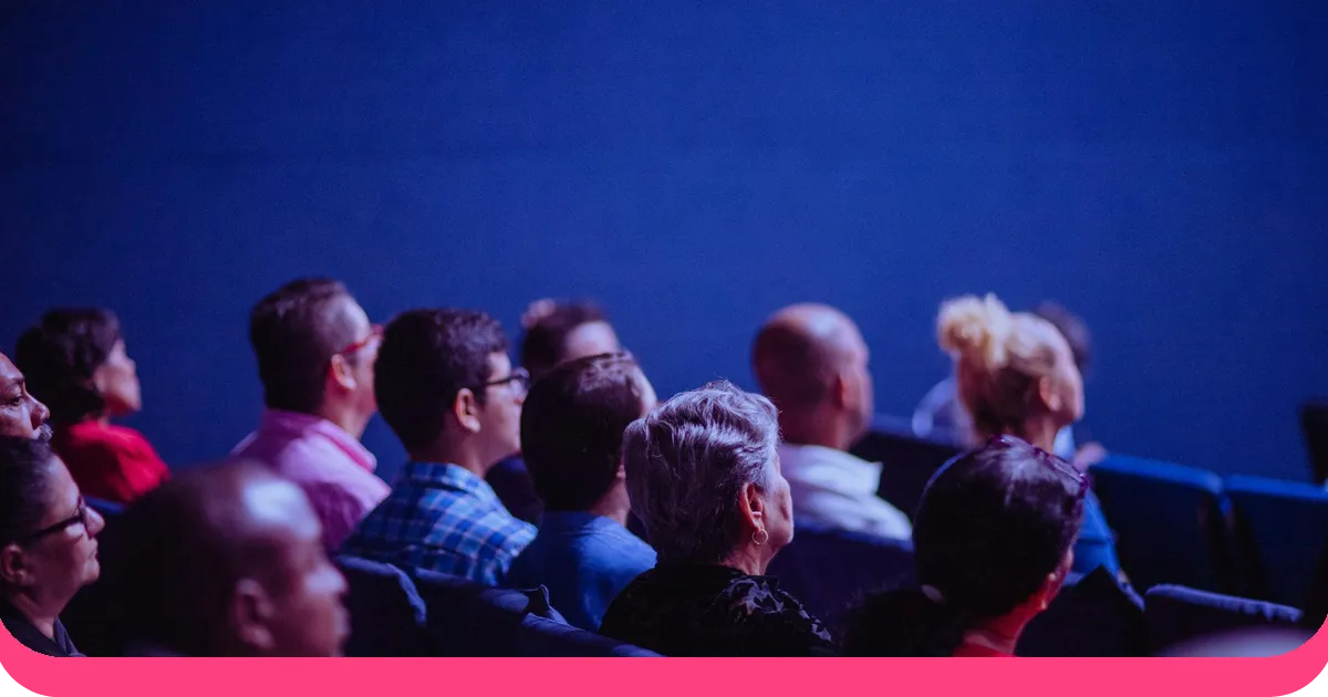 Engaged diverse audience watching a public speaking event in an auditorium with blue stage lighting