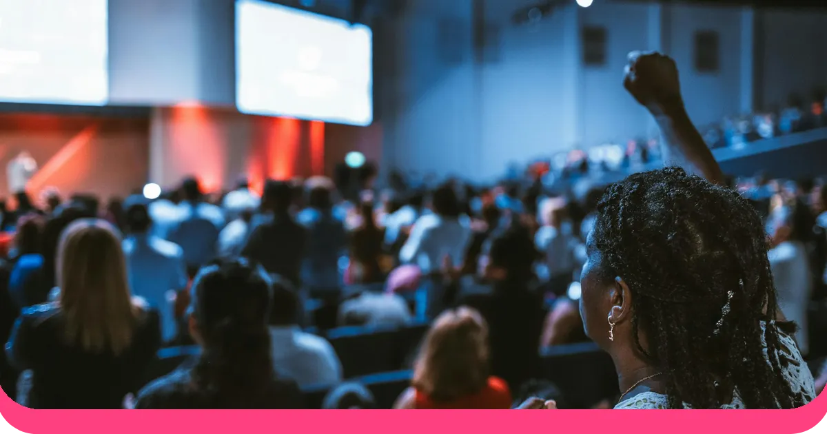 Audience member raising hand during a public speaking event in a large auditorium with stage lighting