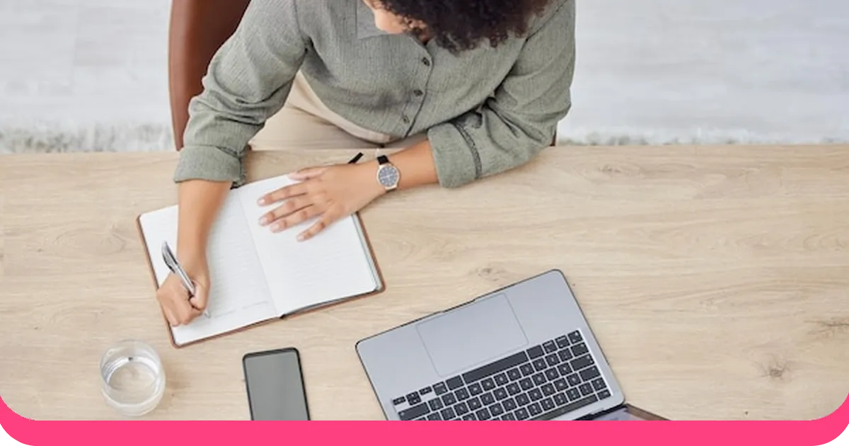 A person writing in a notebook beside a laptop, planning their presentation outline