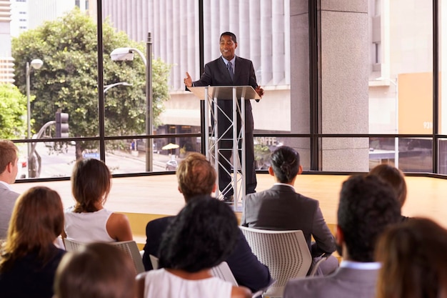 A businessman delivering a sales presentation to a seated audience in a seminar room