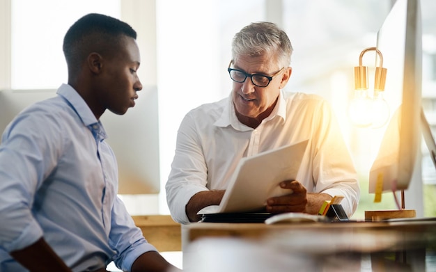 A senior manager mentoring a new employee, reviewing documents together at a desk