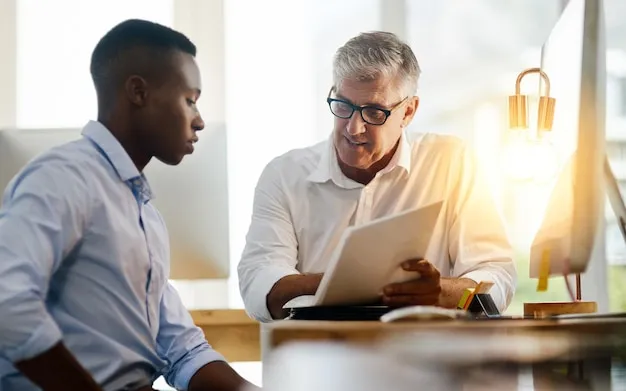 A senior manager mentoring a new employee, reviewing documents together at a desk