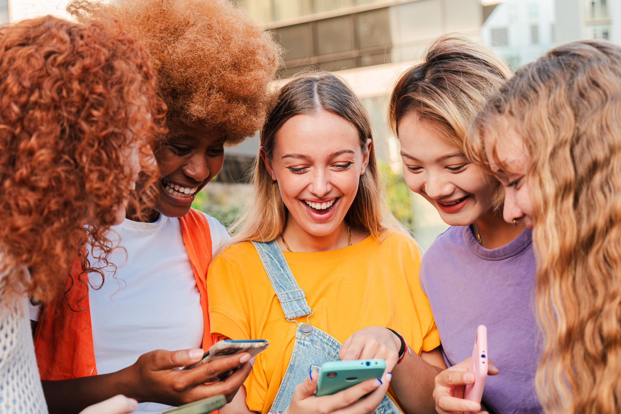 Group of teenagers happily using their smartphones together