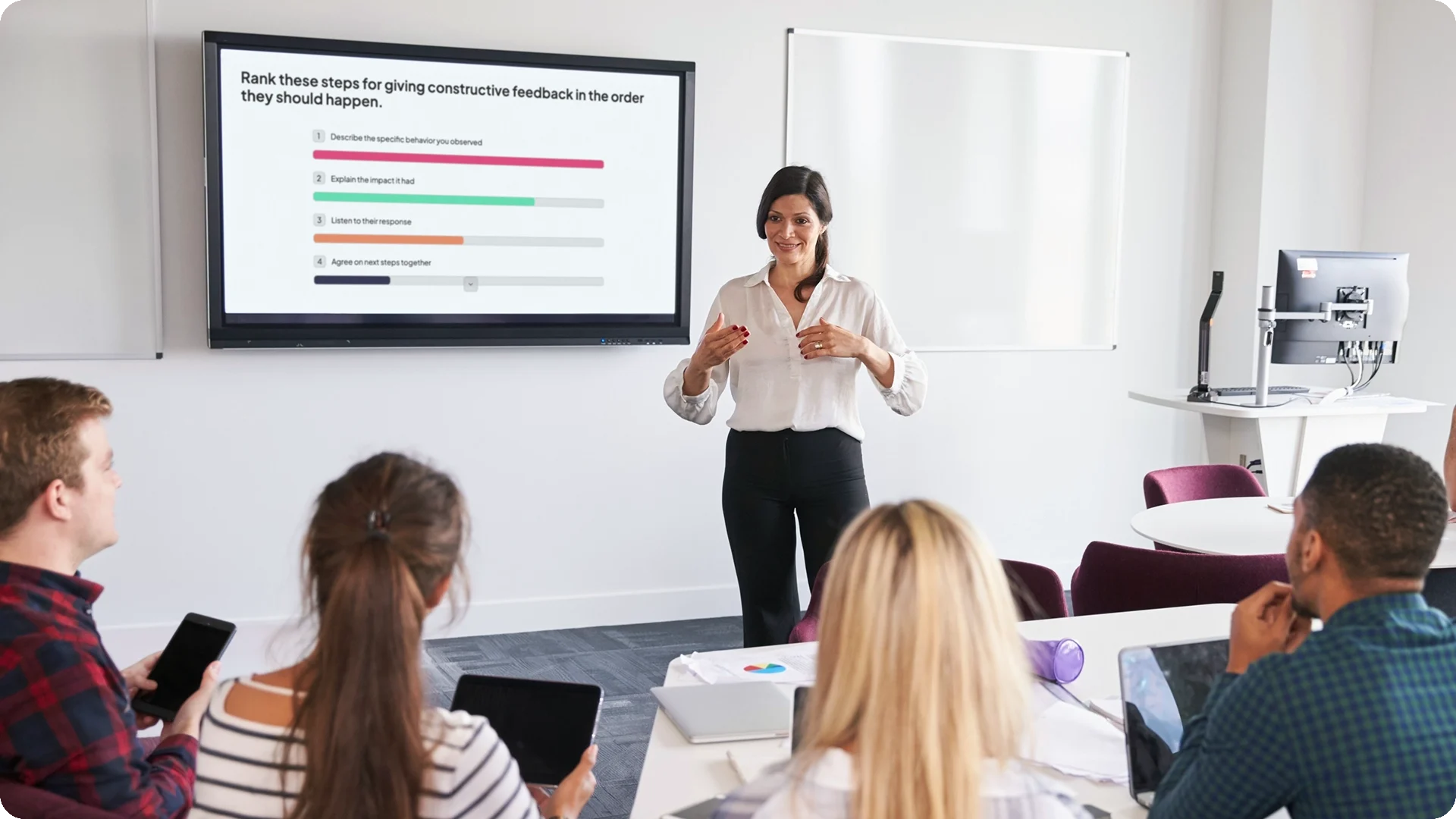 A trainer in front of live ranking poll results, with learners answering on their own phones and tablets